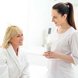 A female nurse standing and speaking to a female patient sitting in her robe